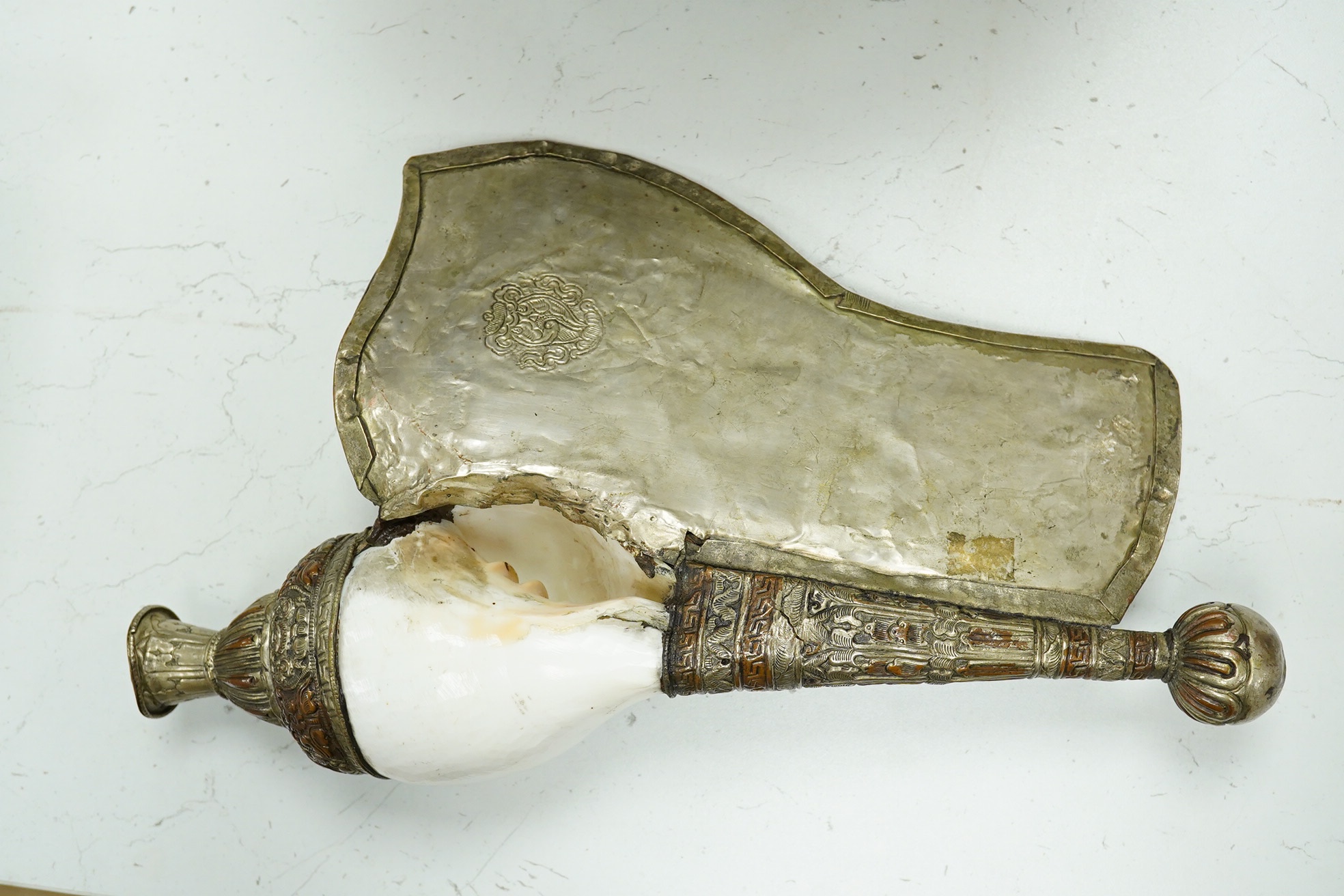 A Tibetan repoussé work cowrie shell trumpet, early 20th century, set with a cabochon, 37cm high. Condition - fair to good